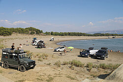 Campingfahrzeuge stehen am Strand an der albanische Reviera, im Bild auch ein Landrover mit Dachzelt