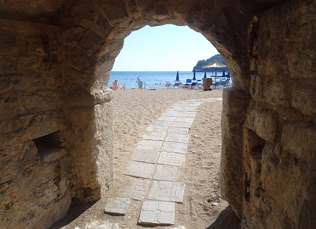 Durch einen steinerner alten Torbogen führt ein Weg hinaus aus der Stadt Budva (Montenegro) hinaus an den Stadtstrand