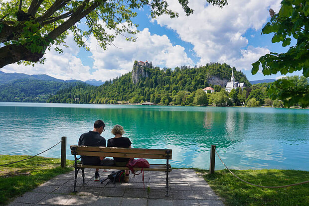 Zwei Menschen sitzen entspannt auf einer Bank am Bleder-See in Bled und blicken aufs Wasser, Bled liegt in Slowenien