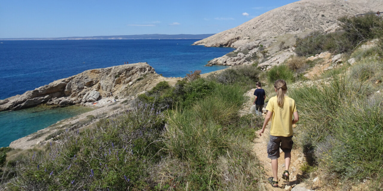 Zwei junge Männer marschieren über die Felsen Richtung Meer in Kroatien