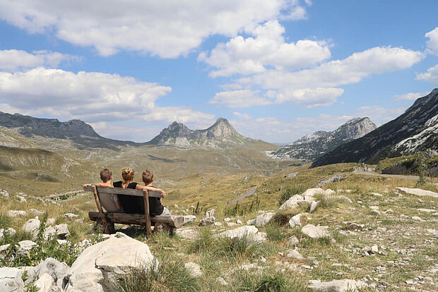 Drei Personen (u.a. Andrea Markand) sitzen auf einer Bank und blicken auf das Durmitor-Gebirge in Montenegro