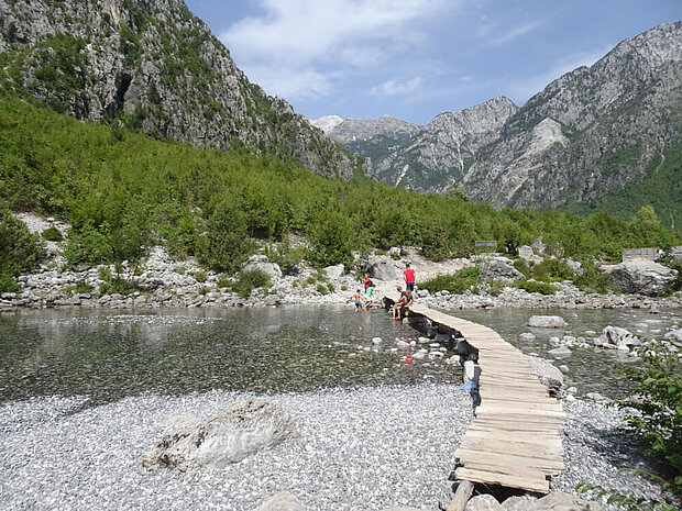 Eijn Steg führt über einen Fluss. Kinder spielen im Wasser. Gegend nahe Thet (Albanien)